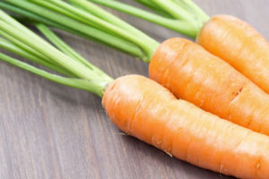 50552346 - raw carrots with green tops on wooden background